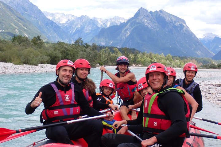 Group of people in red helmets rafting on a river with mountainous landscape in the background.