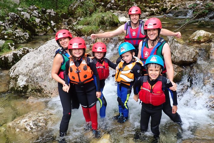 Group of six people in helmets and life vests posing by a rocky stream.